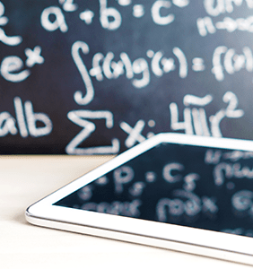 ipad on a desk with a chalkboard with math equations in the background