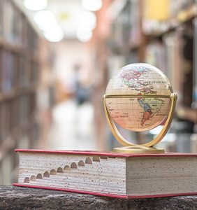 small globe sitting on top of a dictionary in a library